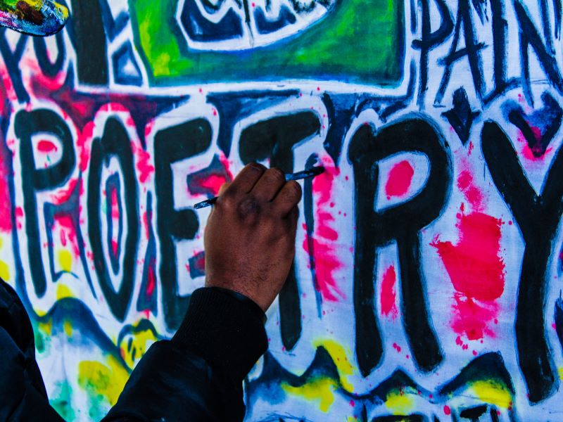 A man’s hand adds paint to a colorful mural that reads “POETRY.”