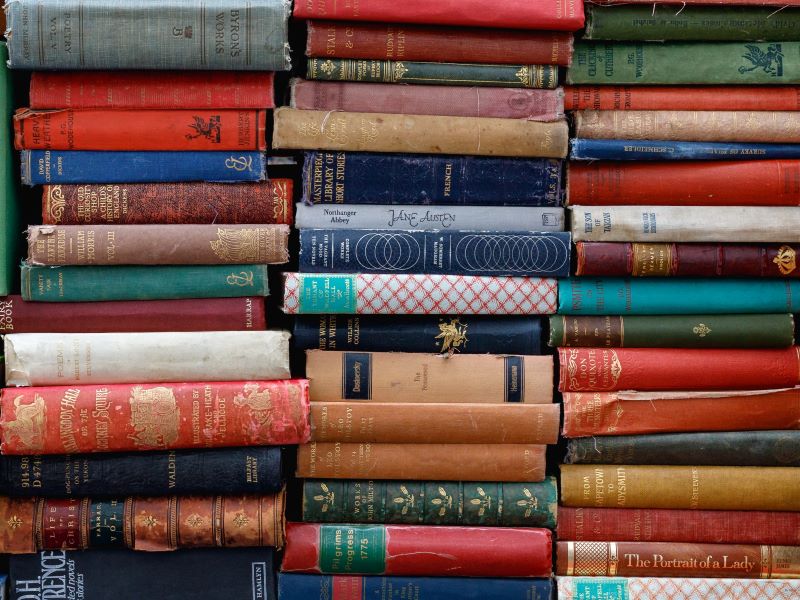 Dozens of colorful books are tightly stacked one on top of the other in three piles standing side by side.