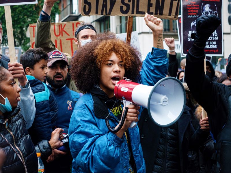 A woman with a bullhorn leads a crowd of protesters as they march down a street.