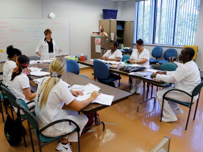 CCAC students in scrubs take notes as an instructor presents to the classroom.